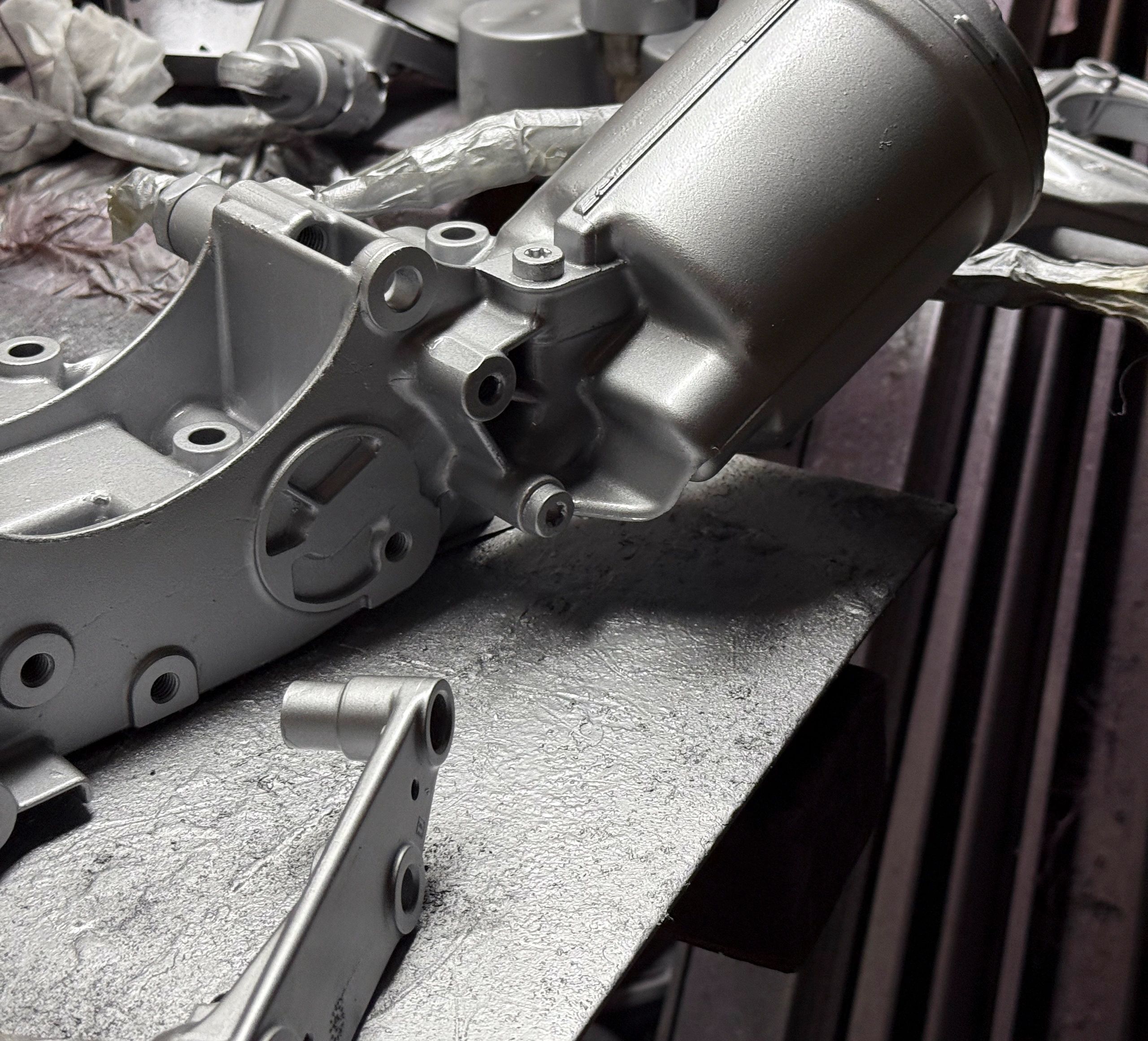 Workers carefully assemble metal parts on a table in a busy workshop, highlighting craftsmanship